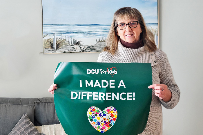 Woman smiling while holding a DCU For Kids sign that reads "I Made a Difference"