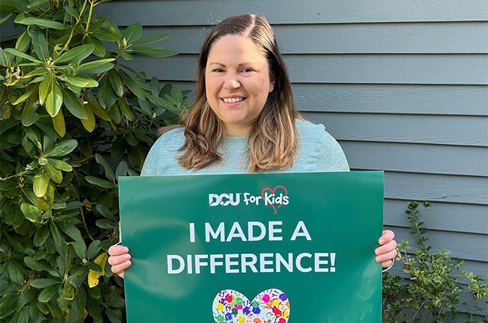 Woman smiling while holding a DCU For Kids sign that reads "I Made a Difference"