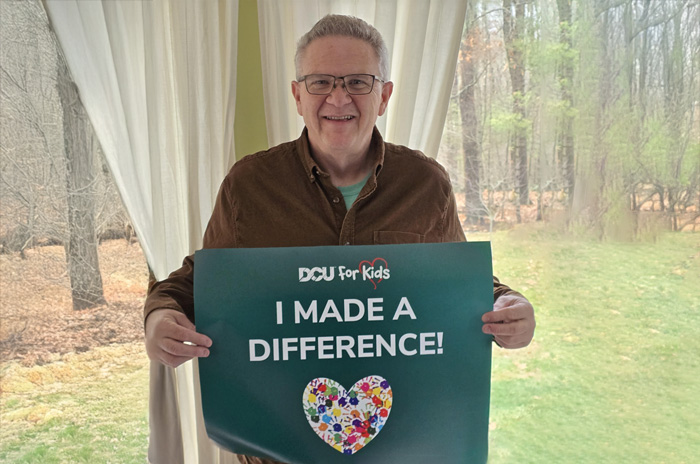 man smiling while holding a DCU For Kids sign that reads "I Made a Difference"