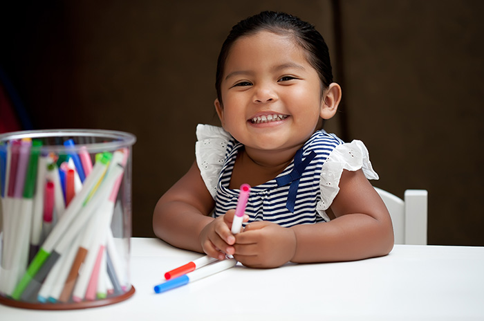 Small child smiling with markers